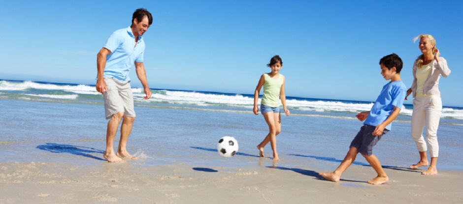 Mum, dad, daughter and son kick a football on the beach